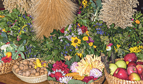 Rund um die Erntekrone liegen Obst, Gemüse, Brot, Nüsse und viele Blumen.