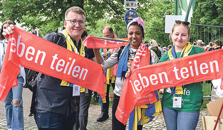 Teilnehmer/innen des Deutschen Katholikentages halten rote Schals mit der Aufschrift „leben teilen“ in die Höhe – dem Motto des Treffens in Stuttgart. 
