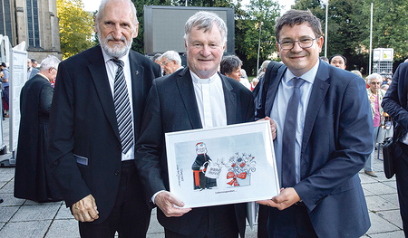 Herausgeber Willi Vieböck und Chefredakteur Heinz Niederleitner gratulierten Bischof Manfred Scheuer mit einer Geburtstagskarikatur von Thomas Wizany.