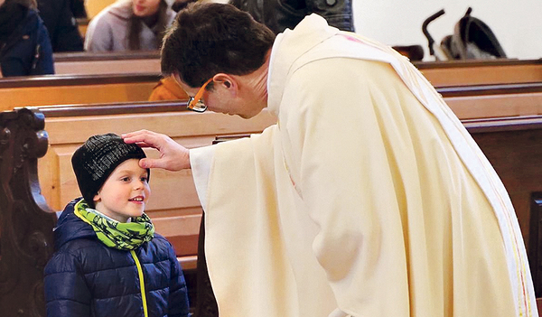 Ein Kreuzzeichen auf die Stirn machen ist eine Form des Segnens. Fabio wird hier von Pfarrer Gert Smetanig in der Pfarrkirche Burgkirchen gesegnet.