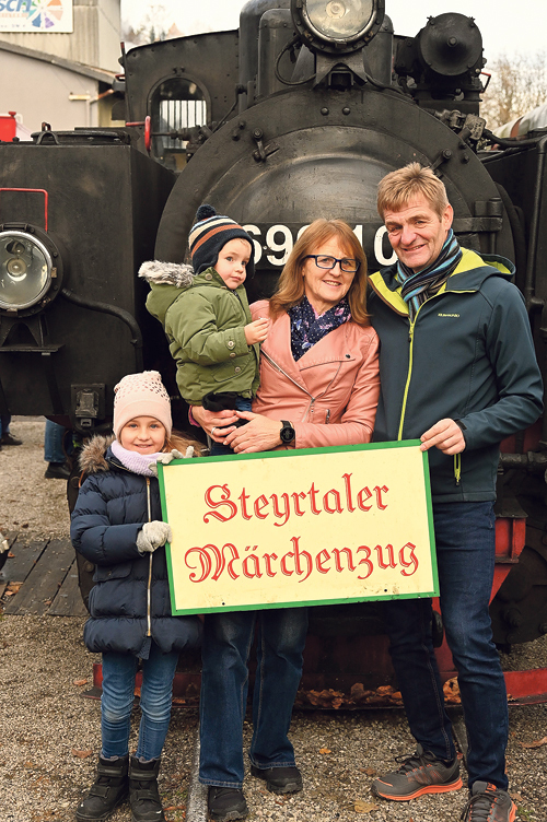 Die Gewinner:innen der Märchenzug-Familienkarte: Lina und Luca mit ihren Großeltern Erna und Karl Reisenberger vor der dampfenden Lokomotive. 