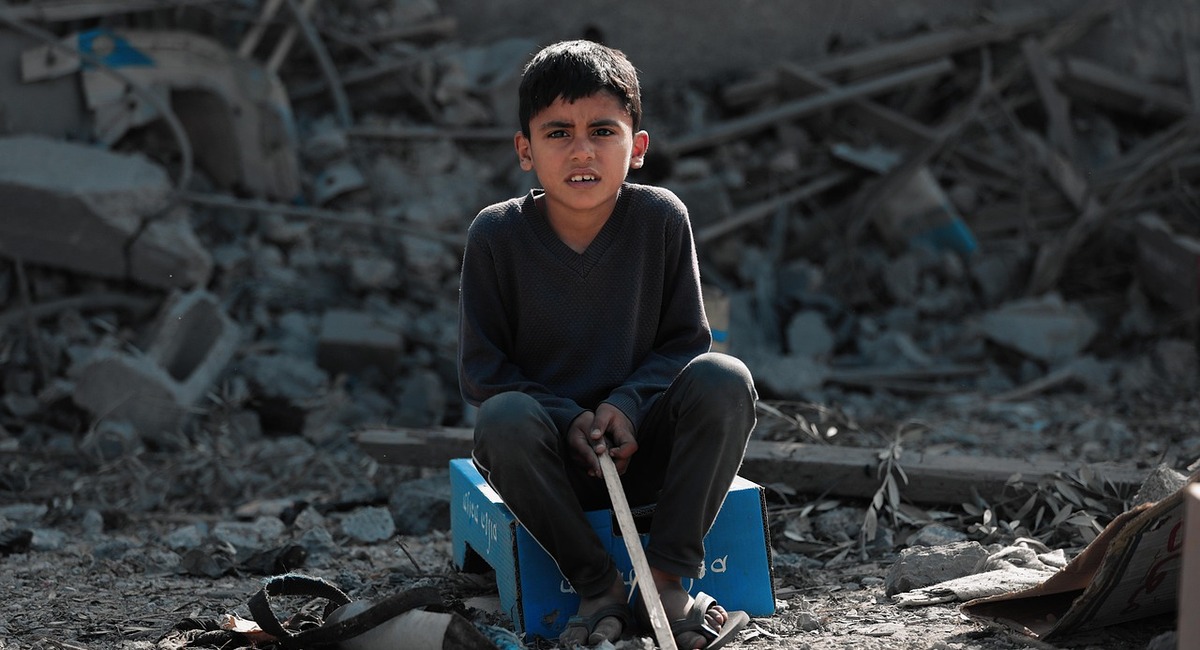 Kleiner Junge der in den Trümmern der zerstörten Häuser in Gaza sitzt.