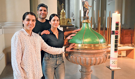 Die drei Taufwerber:innen: Maryam Yami (von links) sowie Masoud Mahyar und Zhara Yavari beim Taufstein ihrer Pfarrkirche „Heilige Familie“ in Linz.   