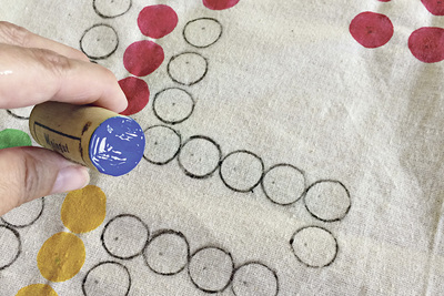 Dann stempelst du mit einem Korken und Stofffarben die bunten Punkte, für die anderen ziehst du mit einem Faserstift Kreise rund um eine Münze.