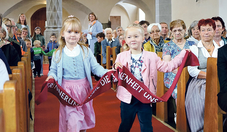 Kinder bringen ein Band mit der Aufschrift „Erinnerung – weil die Vergangenheit uns lehren soll“ zum Altar. 