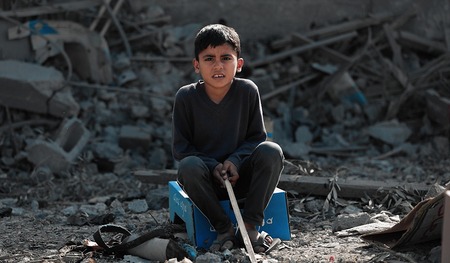 Kleiner Junge der in den Trümmern der zerstörten Häuser in Gaza sitzt.
