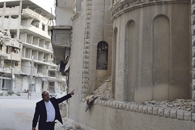 Pfarrer Hanna Ghoneim steht vor der Apsis seiner ehemaligen Kirche.  Der übrige Teil der Kirche ist zerstört. 