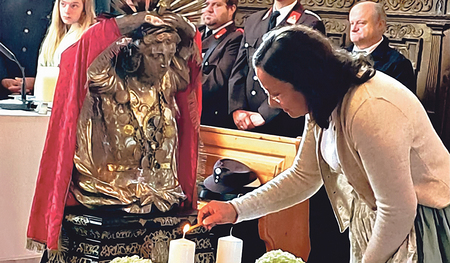 Die Teamleiterin der kfb St. Pantaleon Kathrin Kinzl entzündet Kerzen vor dem ­Reliquiar des heiligen Pantaleon.   