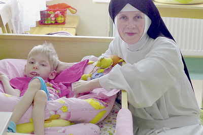 Sr. Simona am Bett der schwerbehinderten Karina im Kinderdorf Gomel für Kinder mit Behinderungen. Es wird von der Caritas OÖ unterstützt.