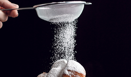 Zucker der durch eine Sieb auf einen Krapfen gestreut wird.