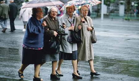 Vier Seniorinnen spazieren mit Regenschirmen bei Regenwetter Arm in Arm auf der Stra?e