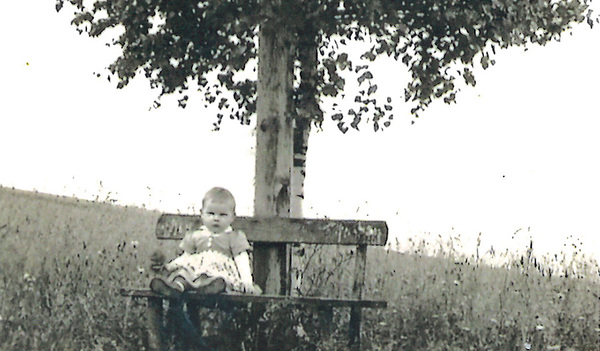 Ein Kind sitzt vor dem Kreuz auf dem Weg zwischen zwei Dörfern. 