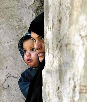 An Iraqi woman holds her child as she looks out her house at the United Nations arms inspection team, before they searched the nearby al-Sawari facility for weapons of mass destruction, 30 km north of Baghdad, December 16, 2002.  U.N. arms teams set 