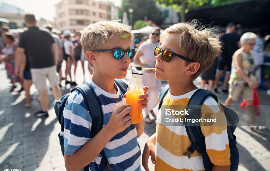 Kids tourists sightseeing town in Majorca. Two young brothers savor the freshly squeezed orange juice in a charming Spanish town. The juice has been prepared at a farmers' market stand, with locally grown oranges. Shot with Nikon D850