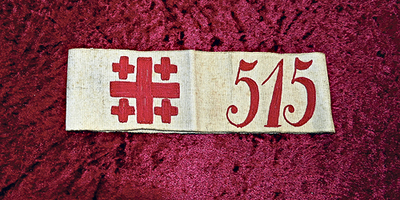 Am Foto unten ist eine Armbinde für Pilger zu sehen: das Jerusalemkreuz und eine Nummer.  