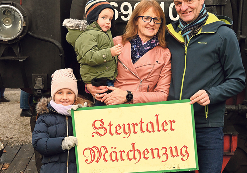 Die Gewinner:innen der Märchenzug-Familienkarte: Lina und Luca mit ihren Großeltern Erna und Karl Reisenberger vor der dampfenden Lokomotive. 