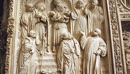 Símeon lobt Gott, als er Jesus im Tempel auf seinen Händen liegen hat (Mitte), links neben ihm steht Maria, rechts die Prophetin Hanna. Joseph ist links unten zu sehen, zu seinen Füßen ein Korb mit zwei Tauben. Relief aus der Kathedrale von Ávia (Spa