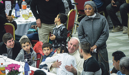 Papst Franziskus sitzt zum Mittagessen am Welttag der Armen, dem 13. November 2022, bei seinen Gästen in der Synodenaula im Vatikan, als ihn ein Mädchen umarmt. 