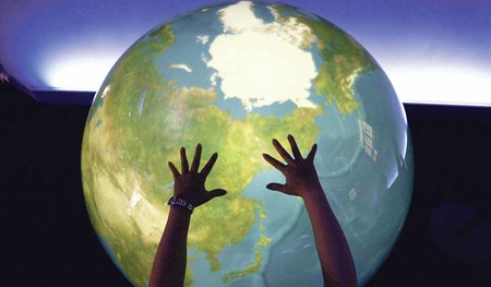 A visitor places her hands on a 'Tangible Earth', a digital globe which real time global metrological data is fed through the Internet from about 300 places in the world, is displayed at an exhibition pavillion inside the media centre for G8 Hokkaido