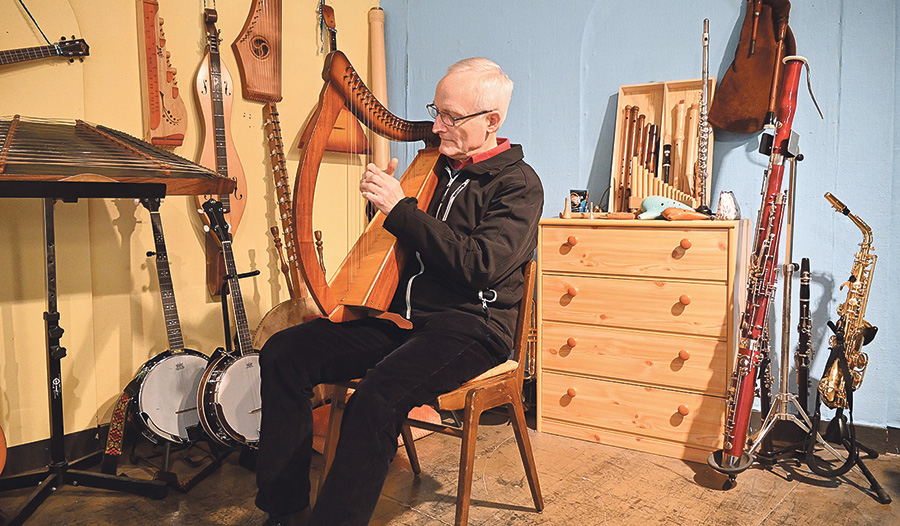 P. Werner Hebeisen spielt auf der Schoßharfe inmitten seiner Instrumente.    